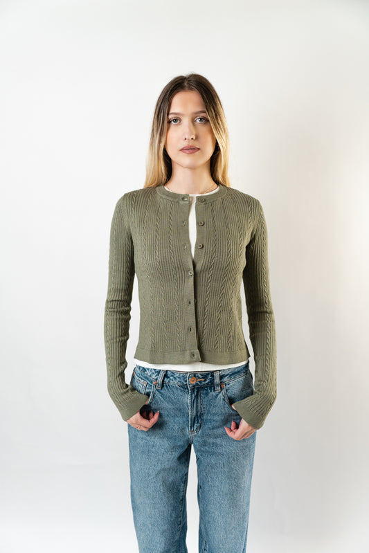 Model wearing the olive Celine Cable Knit Cardigan layered over a white top, shown in a front studio view.