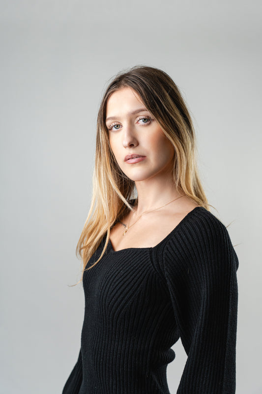 "Close-up of model wearing the black Olivia Ribbed Sweater with a square neckline and ribbed knit texture.