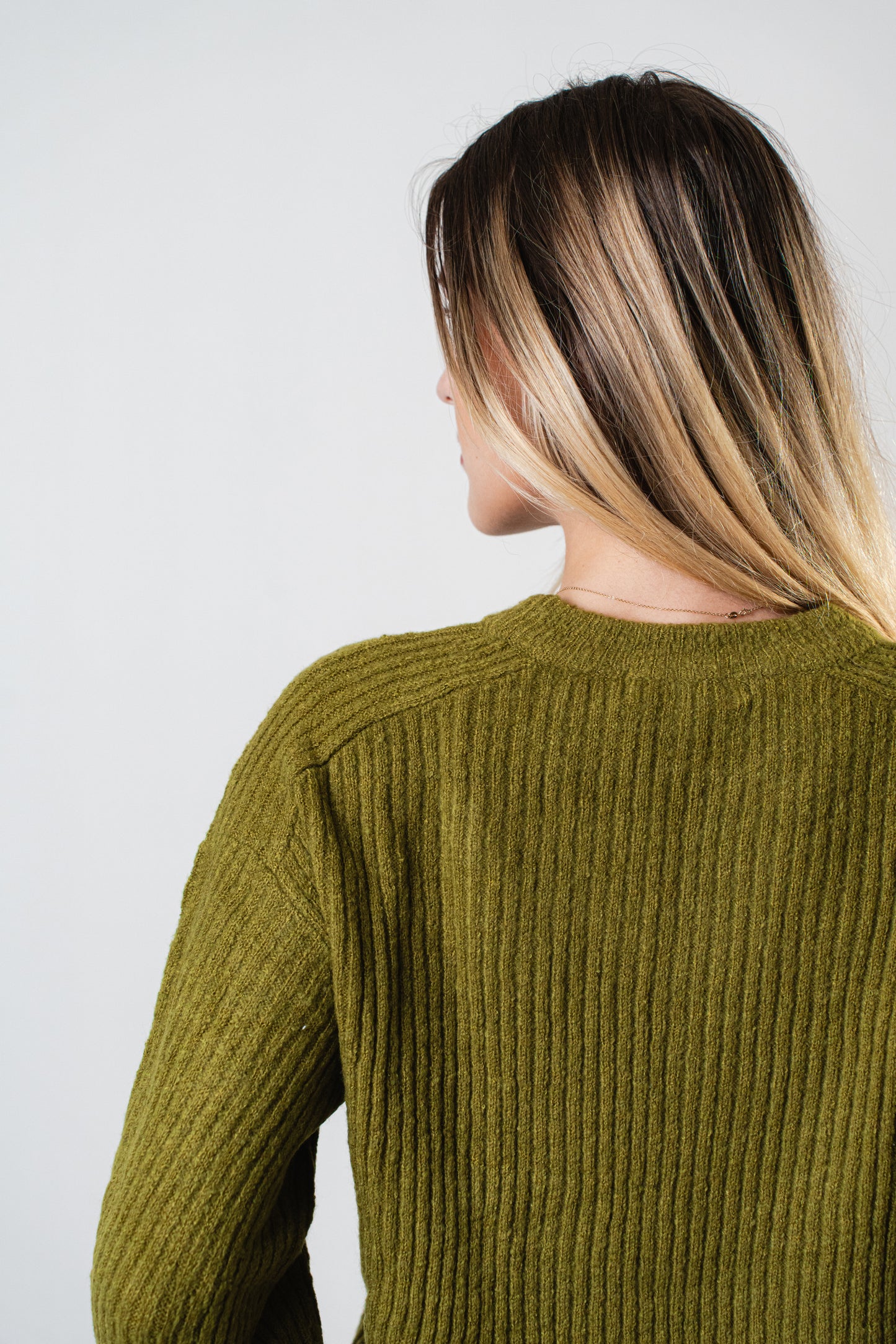 Back view of the model wearing the olive Betty Cooper Ribbed Sweater with a textured ribbed knit design.