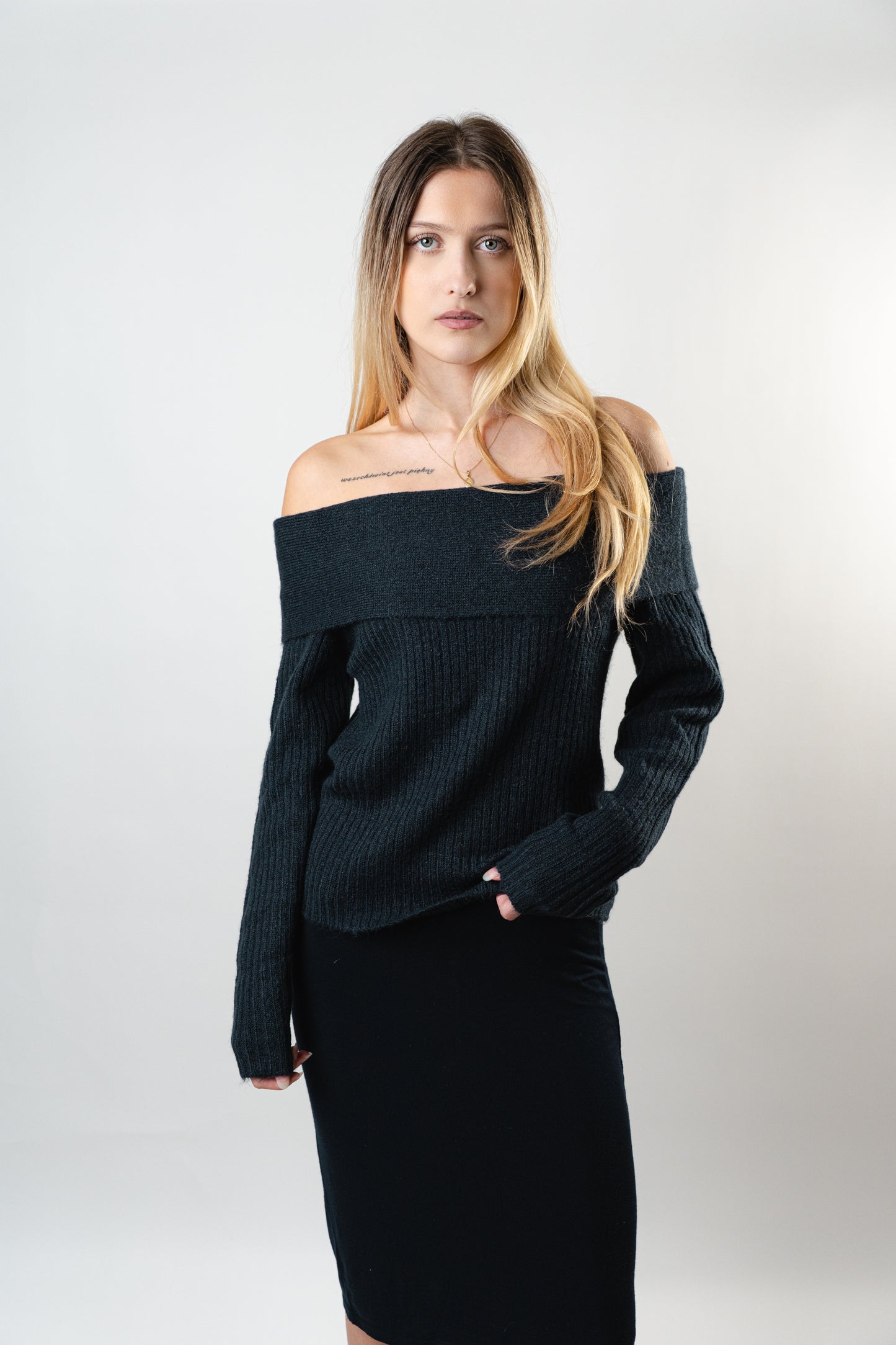 Woman wearing the Amara Off-Shoulder Sweater in black knit, long sleeves, styled in studio on a white background.