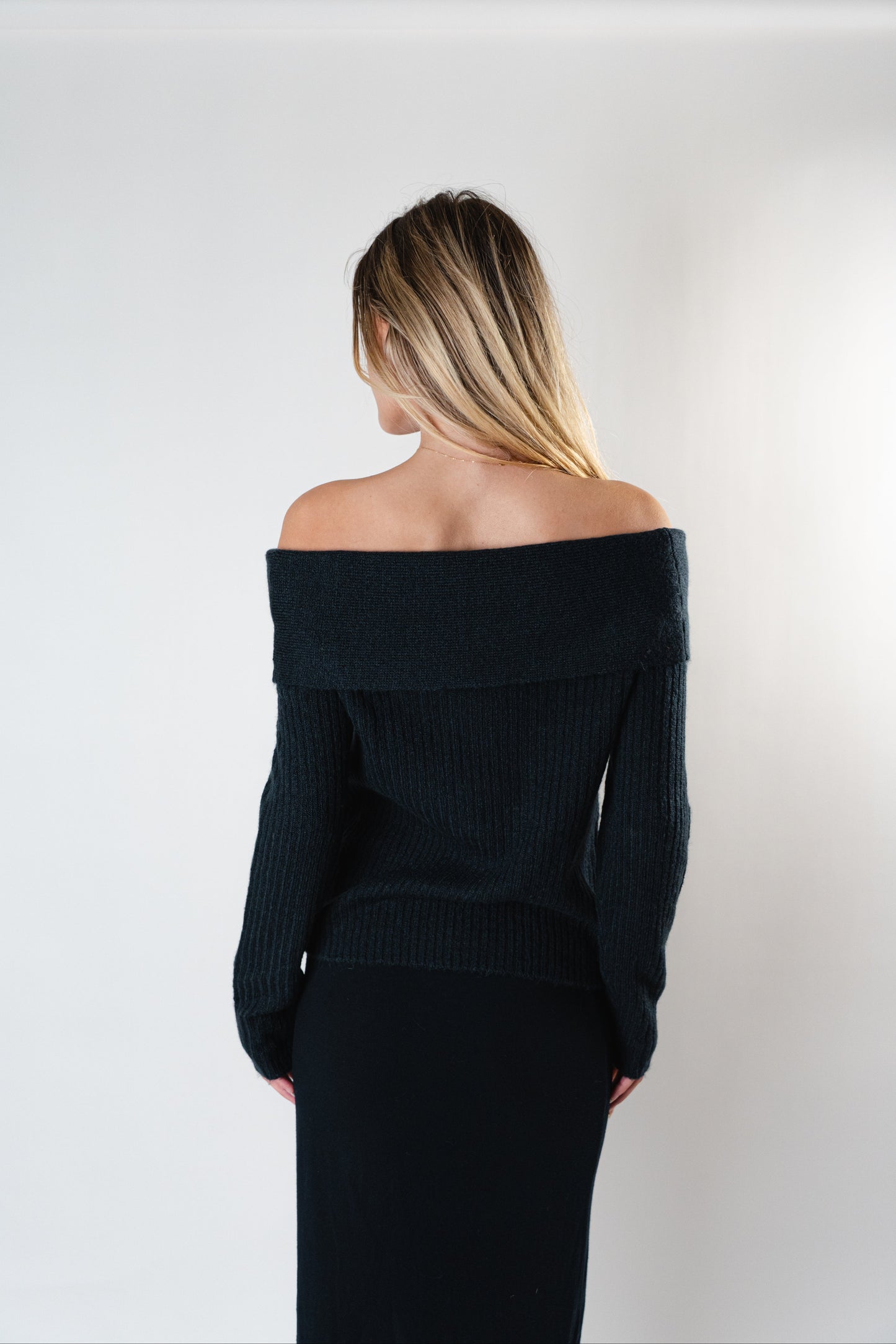 Back view of the black Amara Off-Shoulder Sweater worn by model in a studio.