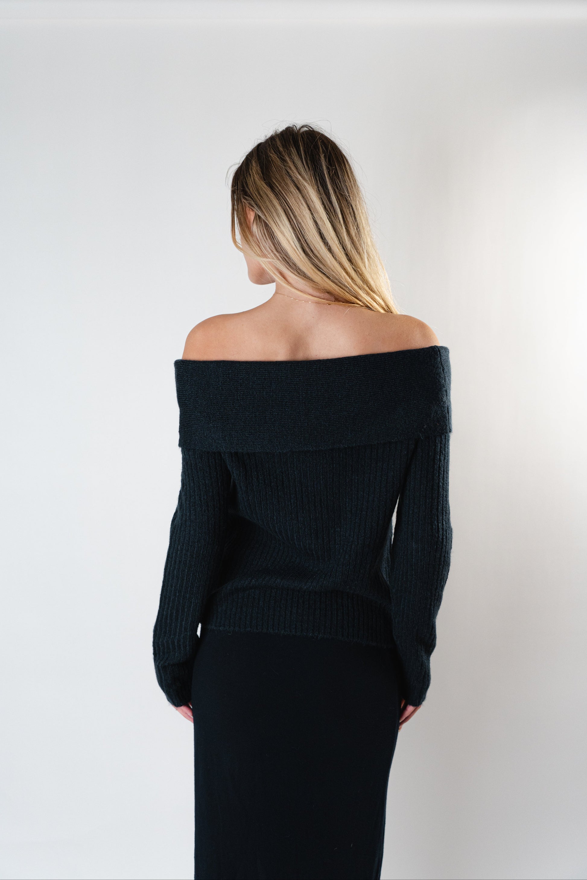 Back view of the black Amara Off-Shoulder Sweater worn by model in a studio.