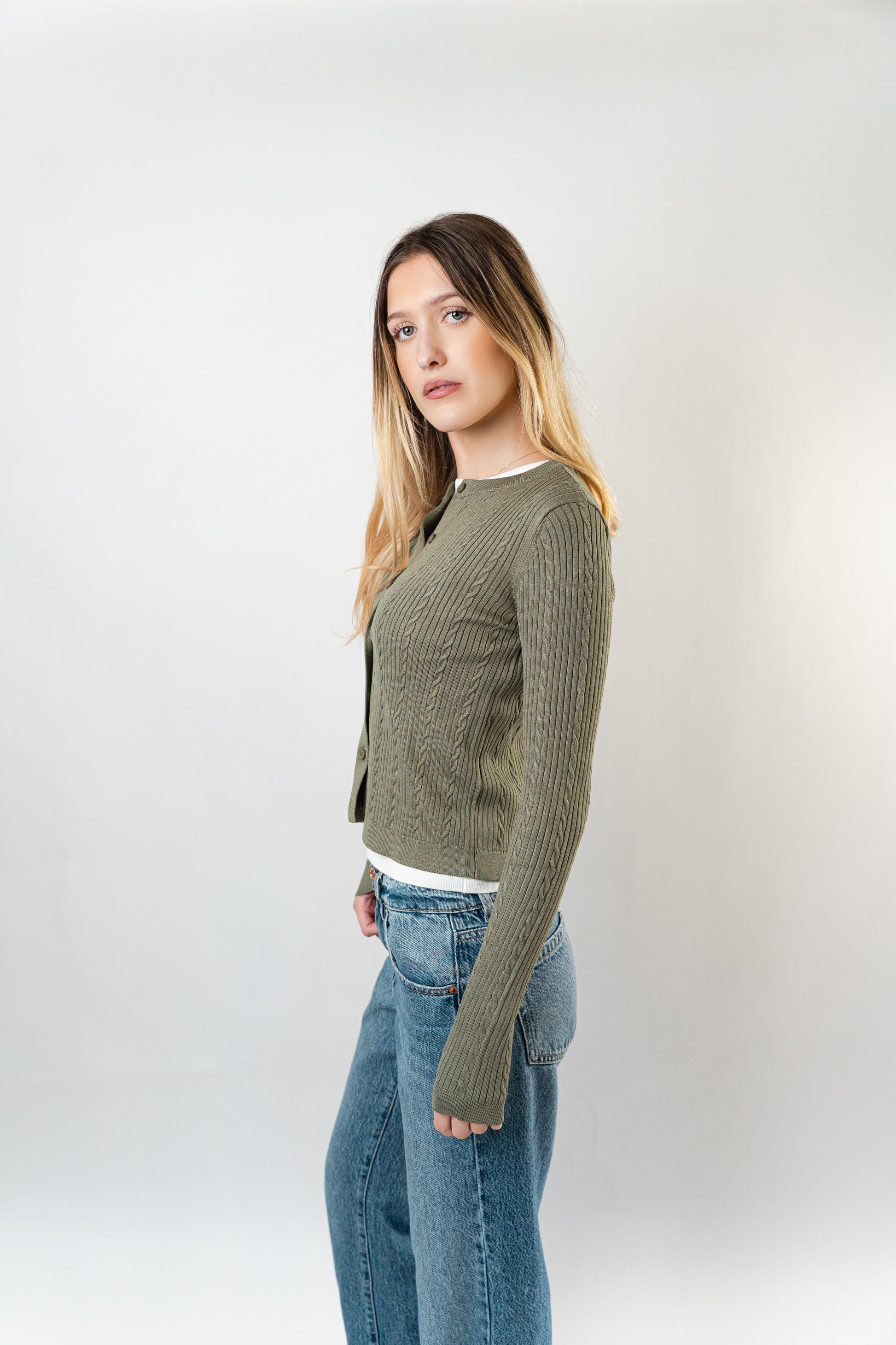 Side view of model wearing the olive Celine Cable Knit Cardigan layered over a white top.