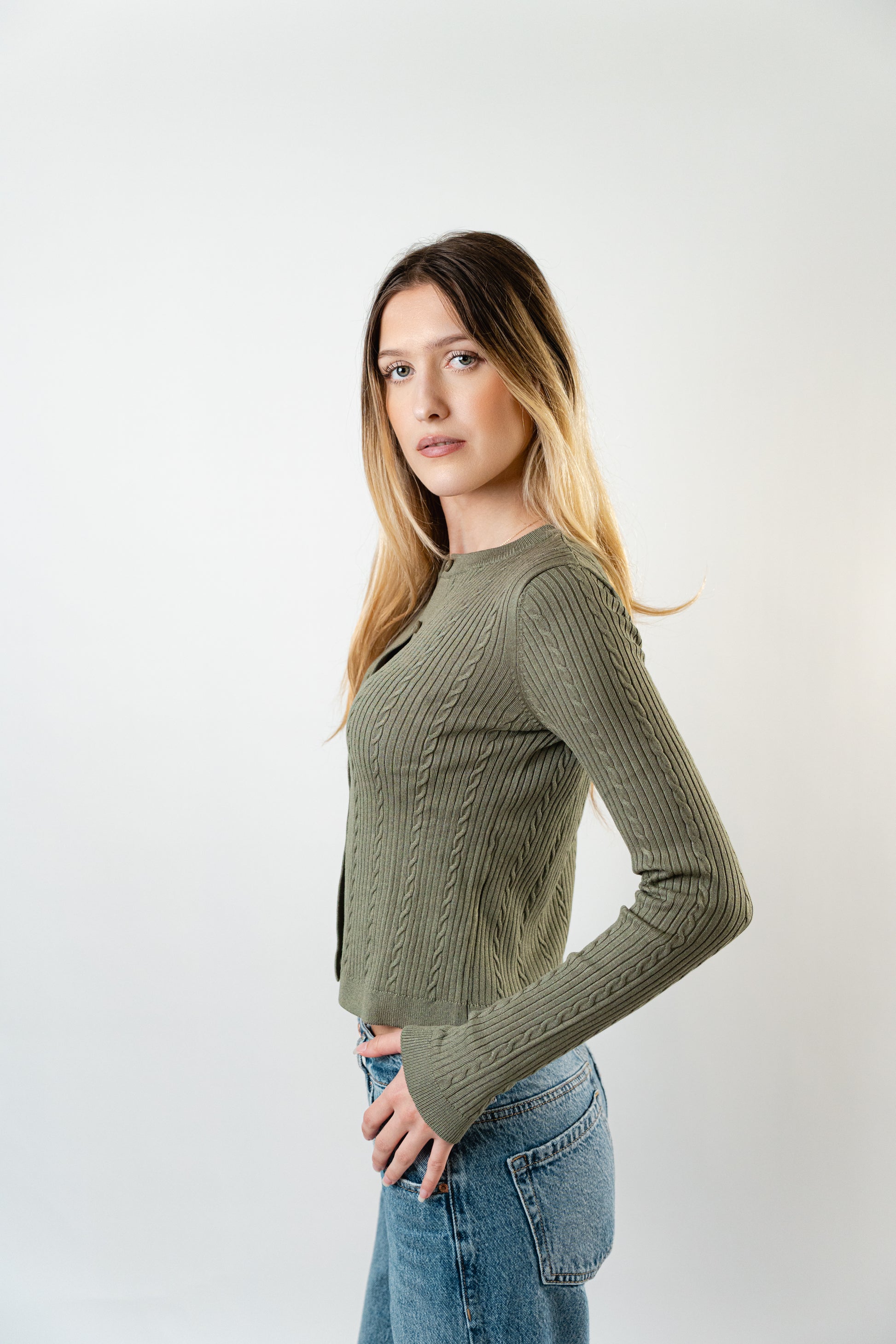 Side view of model wearing the olive Celine Cable Knit Cardigan layered over a white top.