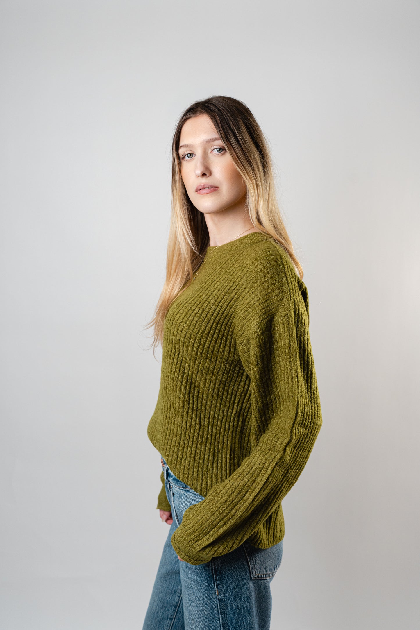 Side view of the model wearing the olive Betty Cooper Ribbed Sweater.
