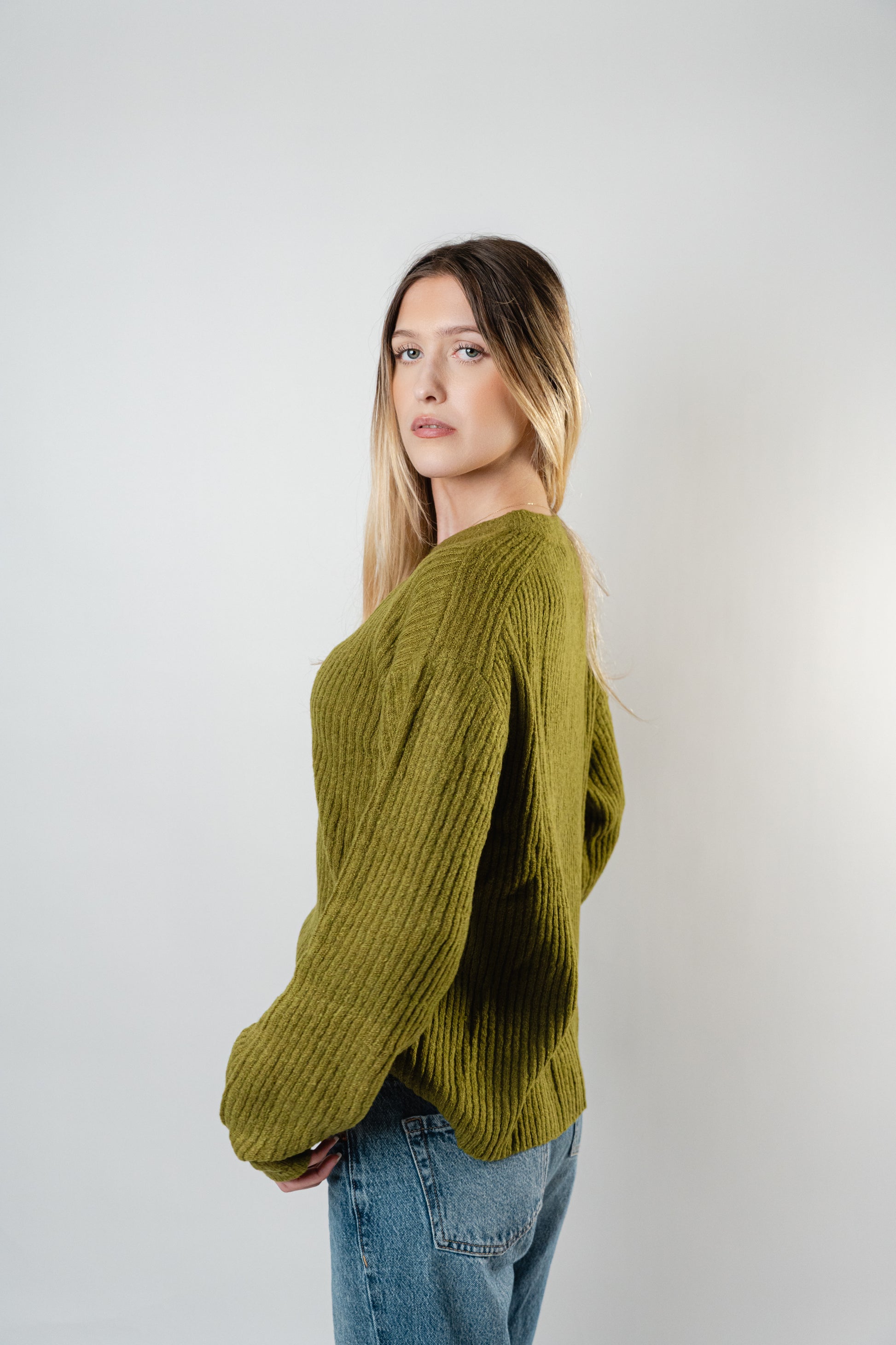 Side view of the model wearing the olive Betty Cooper Ribbed Sweater with a relaxed ribbed knit design.