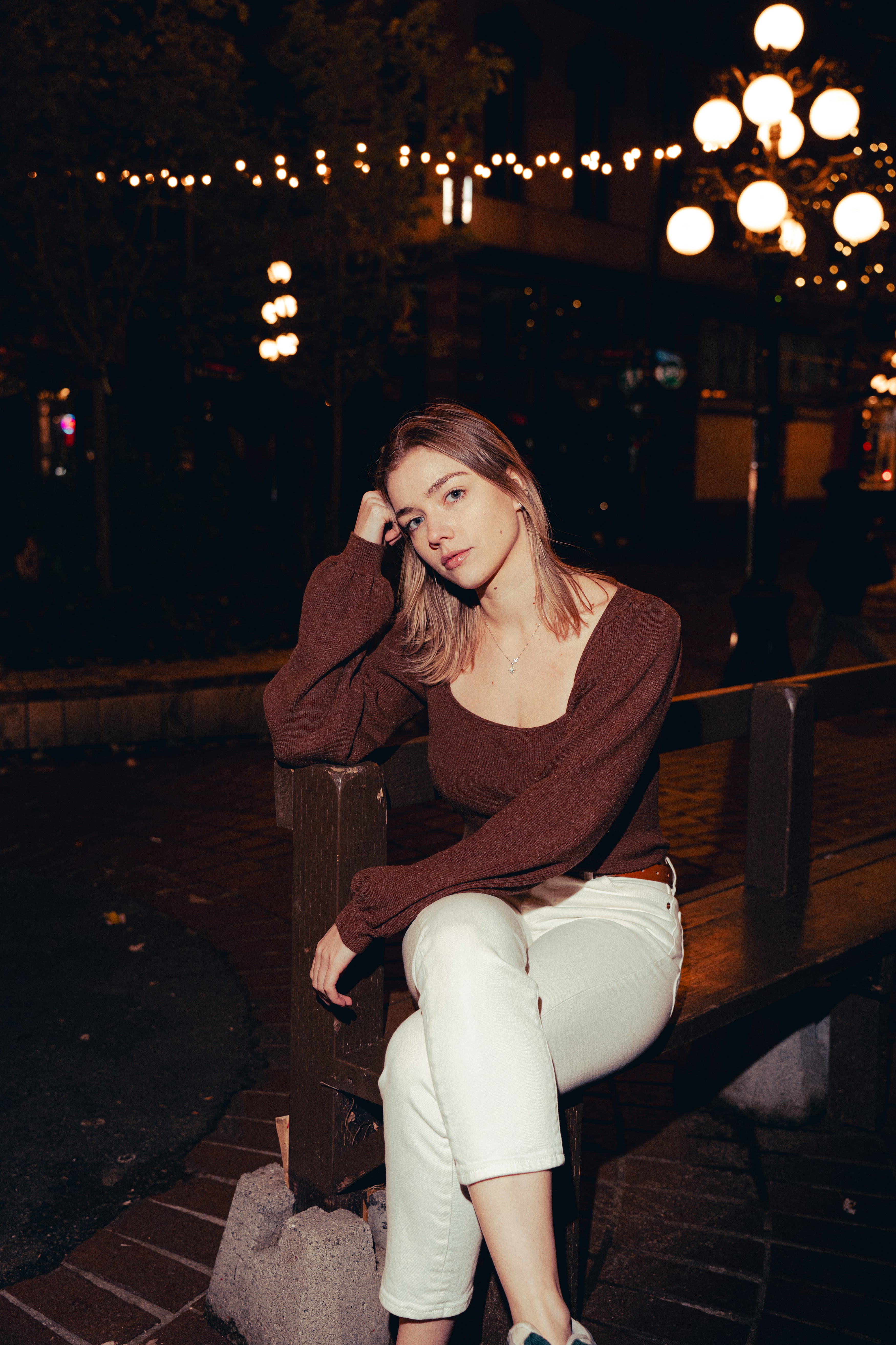 Woman sitting on a bench at night with string lights in the background